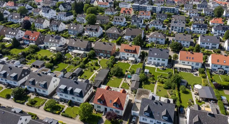 Aerial drone view of typical German residential neighborhood with mixed roof types, red and dark roof tiles, gardens visible, sunny day