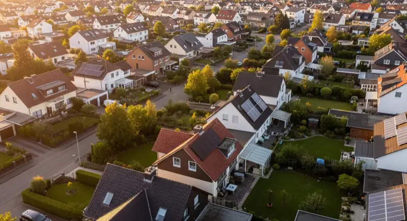 Aerial drone view of typical German residential neighborhood with mixed roof types, red and dark roof tiles, gardens visible, sunny day
