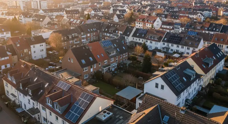 Aerial drone view of typical German residential neighborhood with mixed roof types, red and dark roof tiles, gardens visible, sunny day