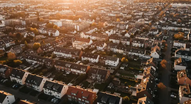 Aerial drone view of typical German residential neighborhood with mixed roof types, red and dark roof tiles, gardens visible, sunny day