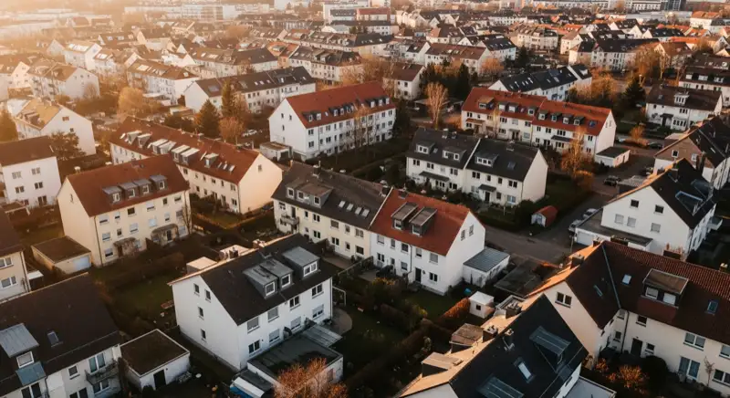 Aerial drone view of typical German residential neighborhood with mixed roof types, red and dark roof tiles, gardens visible, sunny day