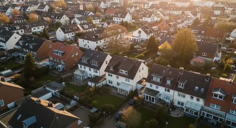 Aerial drone view of typical German residential neighborhood with mixed roof types, red and dark roof tiles, gardens visible, sunny day