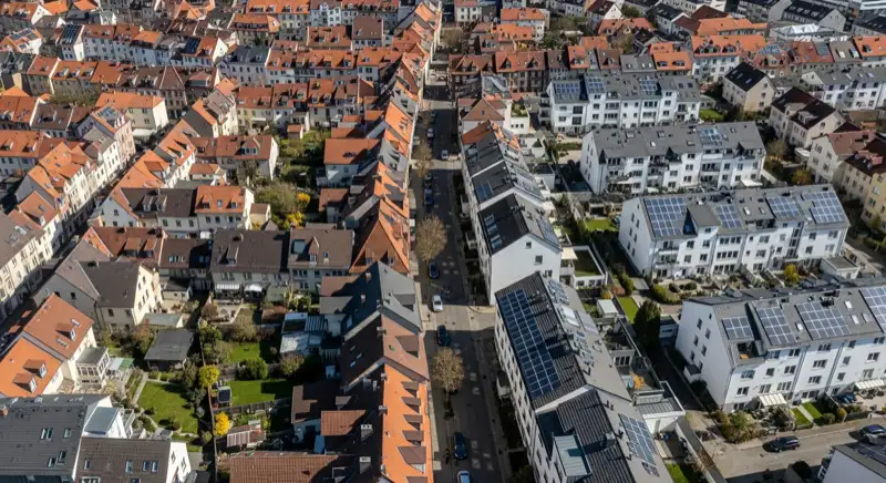 Aerial drone view of typical German residential neighborhood with mixed roof types, red and dark roof tiles, gardens visible, sunny day