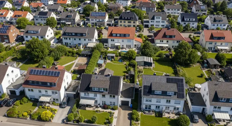 Aerial drone view of typical German residential neighborhood with mixed roof types, red and dark roof tiles, gardens visible, sunny day
