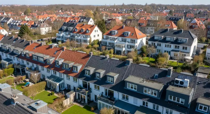 Aerial drone view of typical German residential neighborhood with mixed roof types, red and dark roof tiles, gardens visible, sunny day