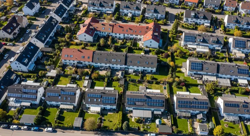 Aerial drone view of typical German residential neighborhood with mixed roof types, red and dark roof tiles, gardens visible, sunny day