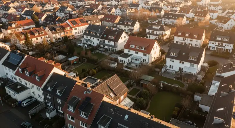 Aerial drone view of typical German residential neighborhood with mixed roof types, red and dark roof tiles, gardens visible, sunny day