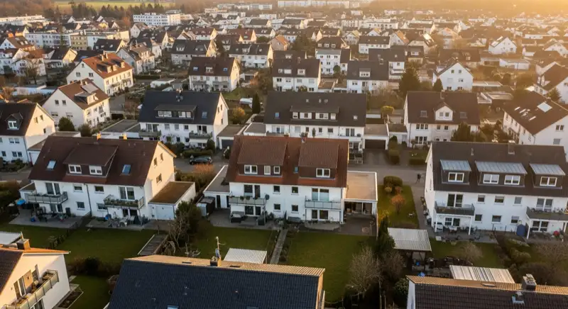 Aerial drone view of typical German residential neighborhood with mixed roof types, red and dark roof tiles, gardens visible, sunny day