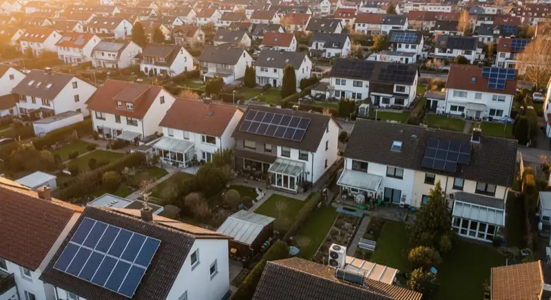 Aerial drone view of typical German residential neighborhood with mixed roof types, red and dark roof tiles, gardens visible, sunny day