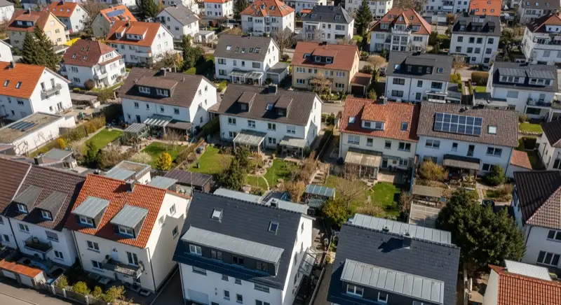 Aerial drone view of typical German residential neighborhood with mixed roof types, red and dark roof tiles, gardens visible, sunny day