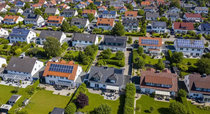 Aerial drone view of typical German residential neighborhood with mixed roof types, red and dark roof tiles, gardens visible, sunny day