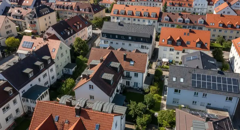 Aerial drone view of typical German residential neighborhood with mixed roof types, red and dark roof tiles, gardens visible, sunny day