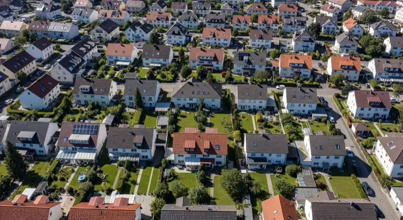 Aerial drone view of typical German residential neighborhood with mixed roof types, red and dark roof tiles, gardens visible, sunny day