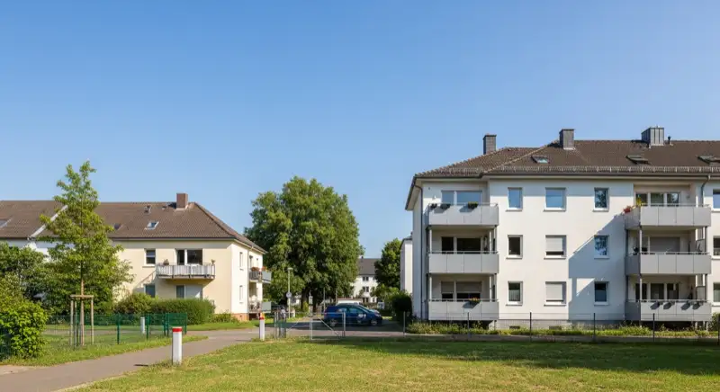 Aerial drone view of typical German residential neighborhood with mixed roof types, red and dark roof tiles, gardens visible, sunny day
