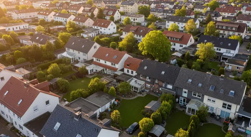 Aerial drone view of typical German residential neighborhood with mixed roof types, red and dark roof tiles, gardens visible, sunny day