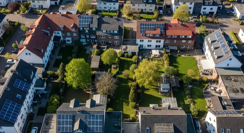 Aerial drone view of typical German residential neighborhood with mixed roof types, red and dark roof tiles, gardens visible, sunny day