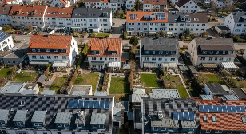 Aerial drone view of typical German residential neighborhood with mixed roof types, red and dark roof tiles, gardens visible, sunny day