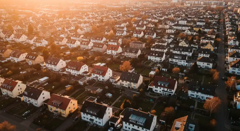 Aerial drone view of typical German residential neighborhood with mixed roof types, red and dark roof tiles, gardens visible, sunny day