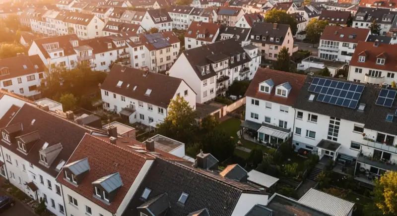 Aerial drone view of typical German residential neighborhood with mixed roof types, red and dark roof tiles, gardens visible, sunny day