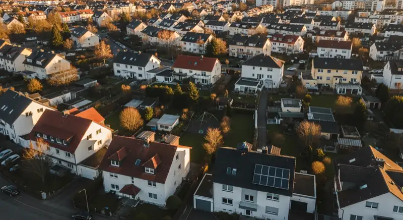 Aerial drone view of typical German residential neighborhood with mixed roof types, red and dark roof tiles, gardens visible, sunny day